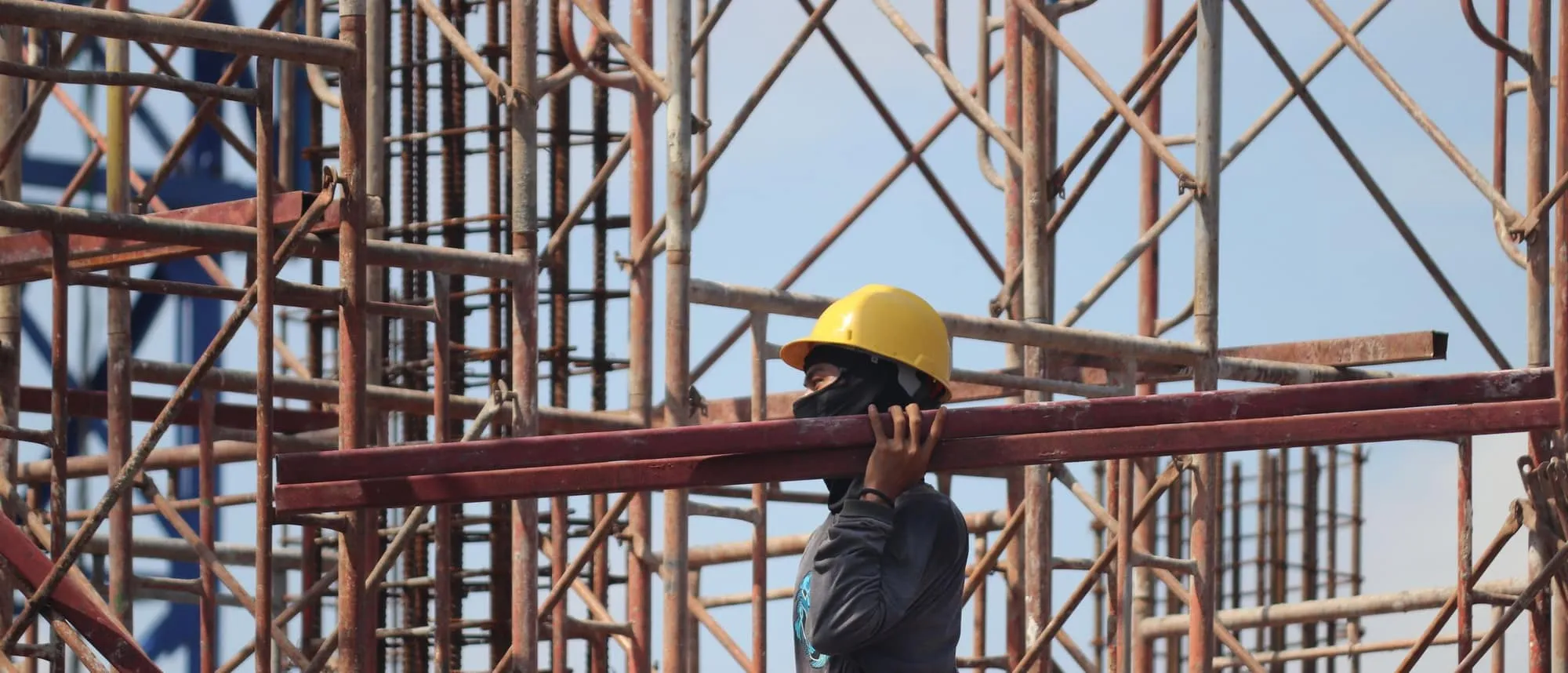 A worker carrying a metal beam across a construction site