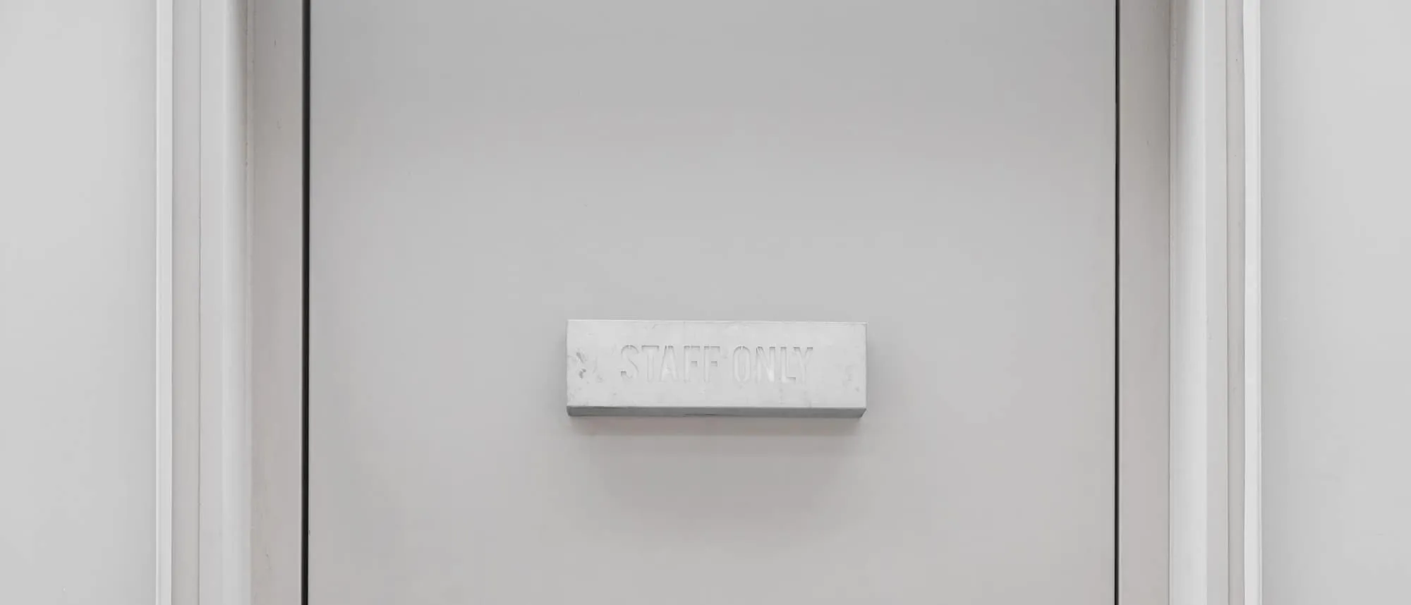 An engraved staff door plate mounted on a plain white office door