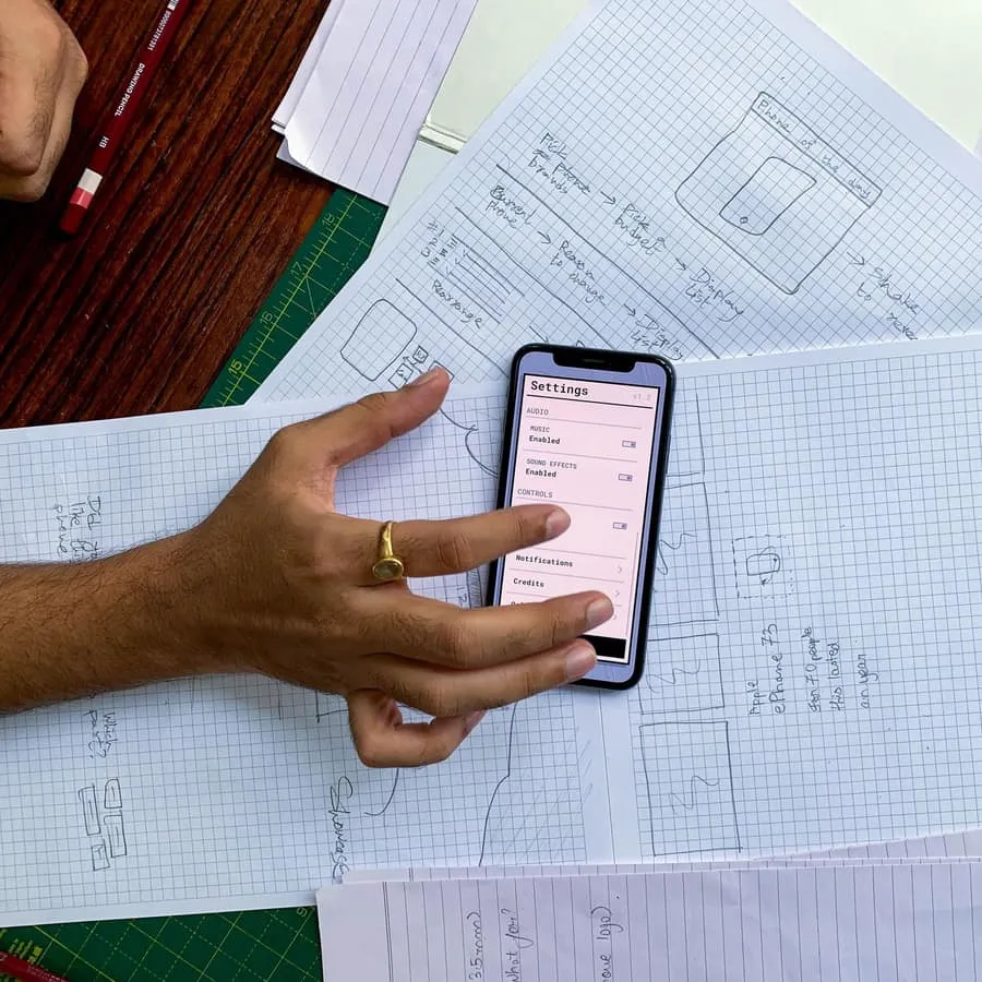 A hand holding a phone over design sketches on paper
