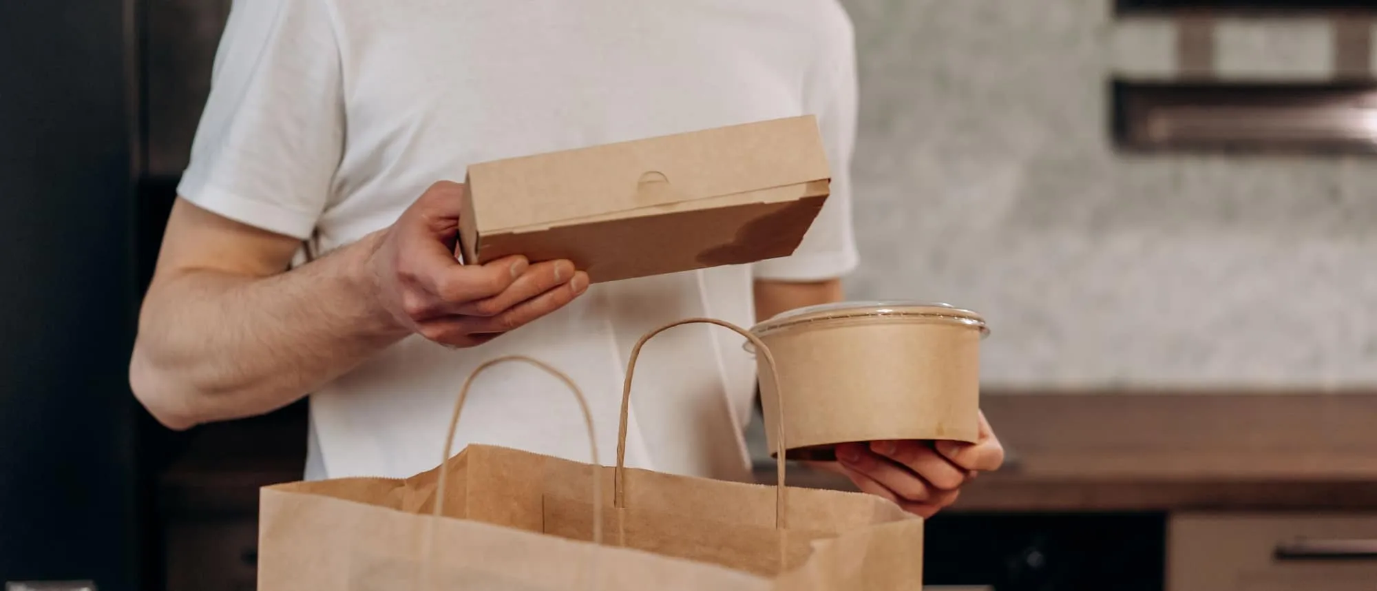 Kraft takeaway boxes and paper bags being handed across a counter