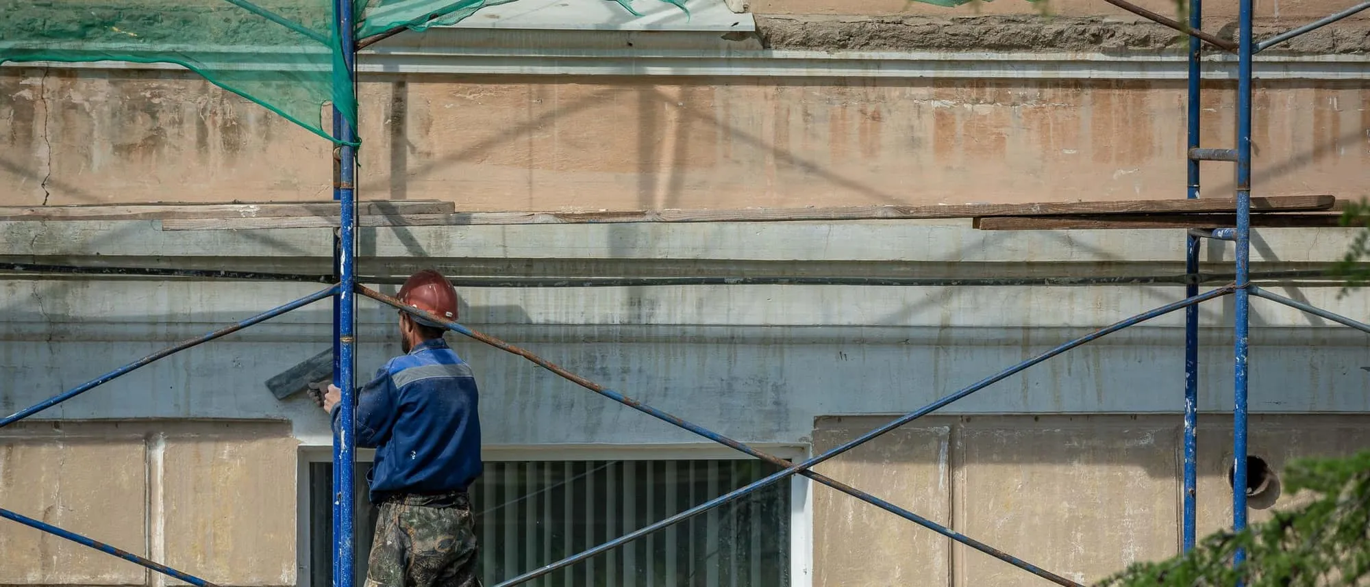 A worker in a hard hat on scaffolding against a building facade