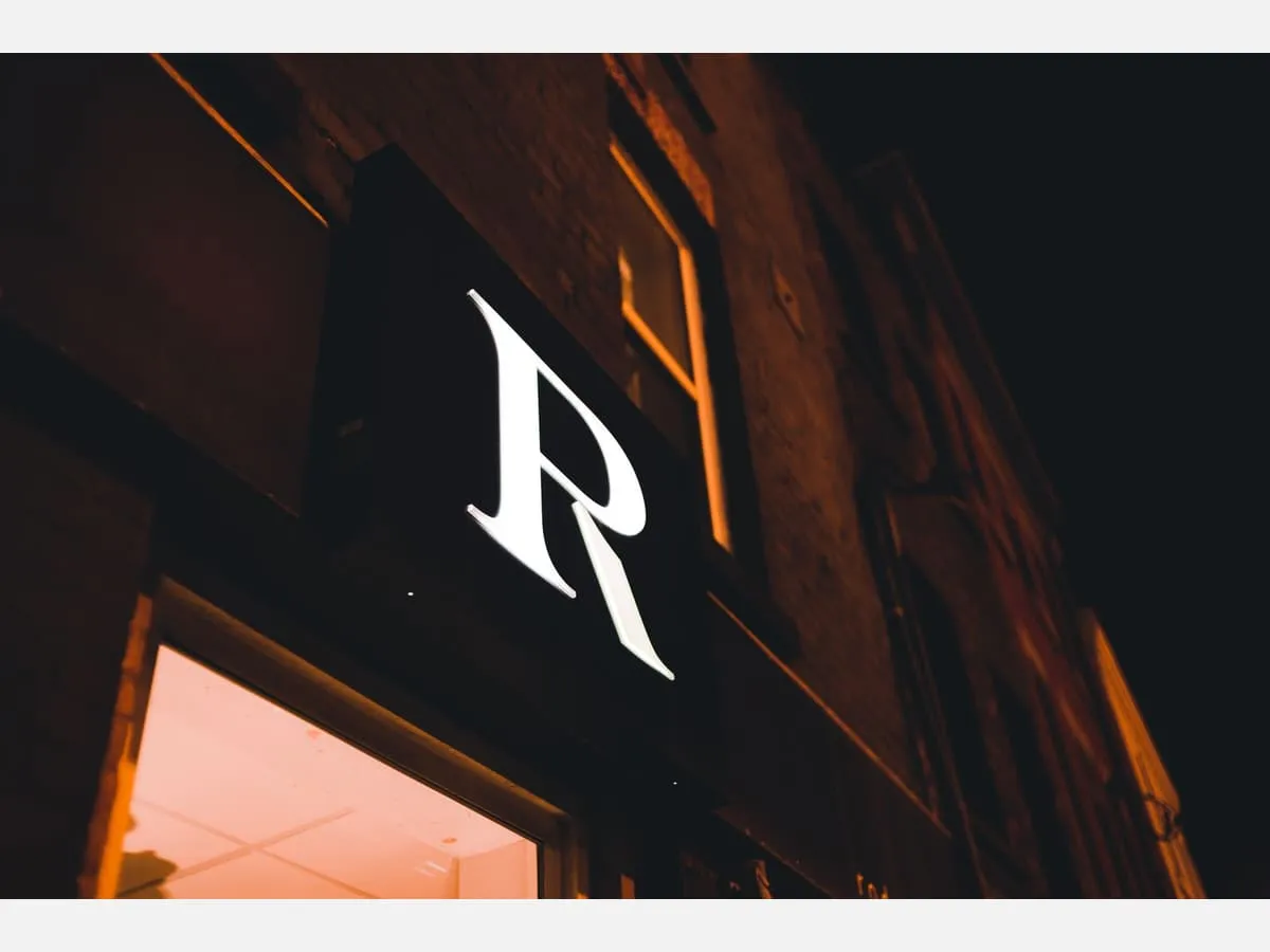 A single backlit letter glowing against a dark facade at night